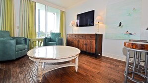 A living room with a round white table, a green sofa, a wooden cabinet, and a TV mounted on the wall. - Six Palms Dreamin 2 Bedroom Condo By Coastal Dreamin (Santa Rosa Beach)
