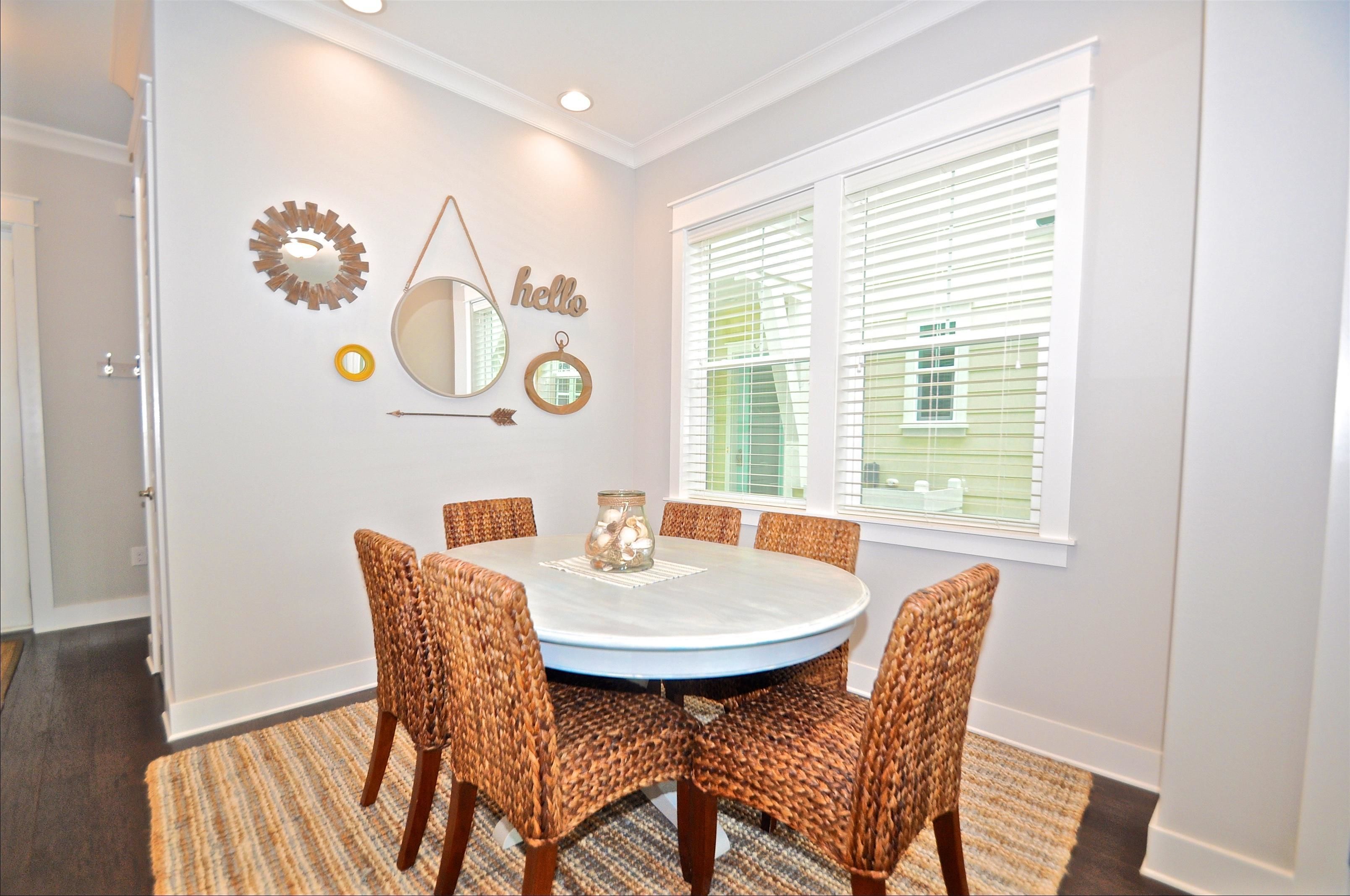 A dining area with a round table, six wicker chairs, a mirror, and wall decorations including a 'hello' sign and a circular mirror.