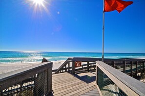 A wooden boardwalk leading to a beach with a lifeguard flag and a warning sign. - Sandlot 3 Bedroom Condo By Coastal Dreamin (Santa Rosa Beach)