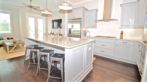 A modern kitchen with white cabinetry, stainless steel appliances, and a central island with bar stools. - Sandlot 3 Bedroom Condo By Coastal Dreamin (Santa Rosa Beach)