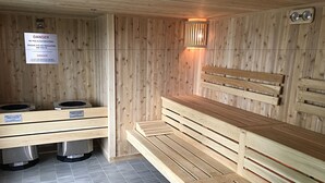 A sauna room with wooden benches and a bench with a backrest. There are two benches with labels indicating the temperature and safety warnings.