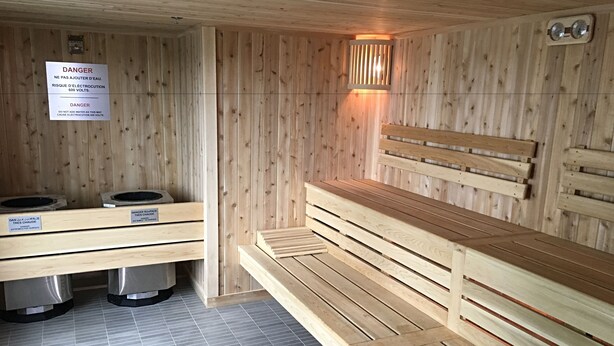 A sauna room with wooden benches and a bench with a backrest. There are two benches with labels indicating the temperature and safety warnings.