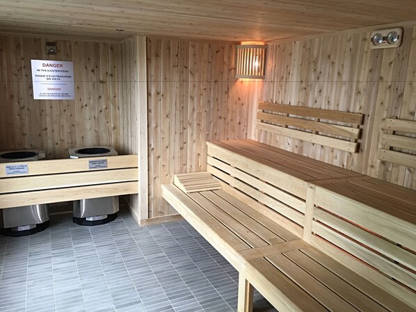 A sauna room with wooden benches and a bench with a backrest. There are two benches with labels indicating the temperature and safety warnings. - Holiday Inn Hotel & Suites Montreal Centre-ville Ouest by IHG (Montreal)