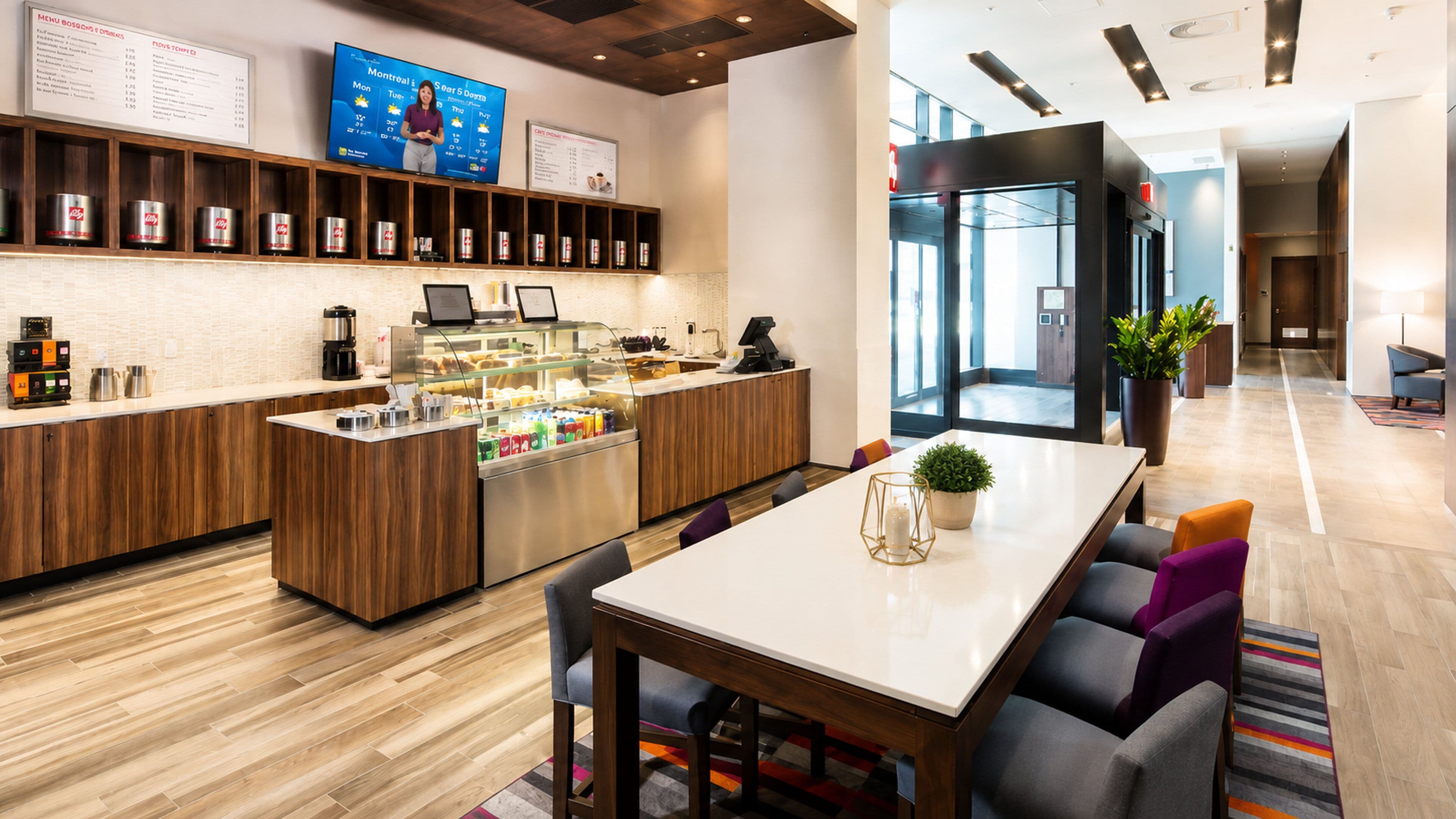 Un moderno vestíbulo de hotel con una recepción, una estación de café y una zona de estar con mesa y sillas.