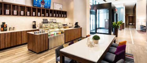 Un moderno vestíbulo de hotel con una recepción, una estación de café y una zona de estar con mesa y sillas.