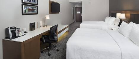 A hotel room with a desk, two beds, a TV, and a coffee maker.