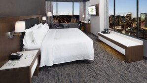 A modern hotel room with a large bed, a desk, and a view of the cityscape.