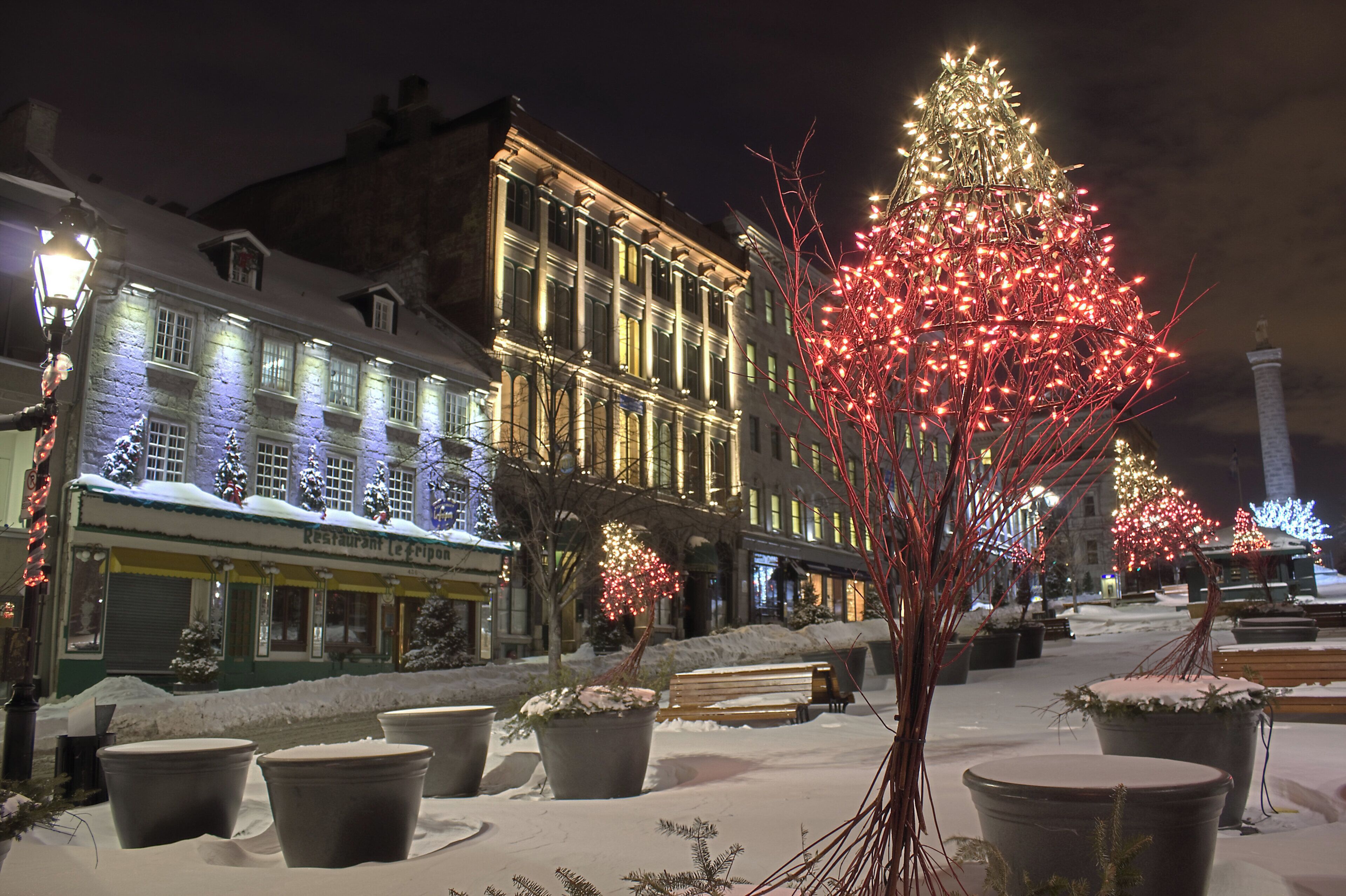 Una calle nevada con edificios iluminados y un árbol decorado.