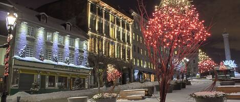 Una calle nevada con edificios iluminados y un árbol decorado.