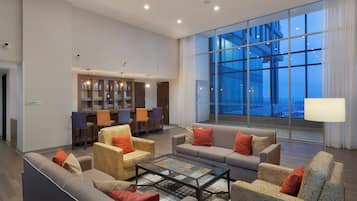 Eine geräumige Lobby mit einer Sitzecke, einer Bar und großen Fenstern mit Blick auf die Stadt.