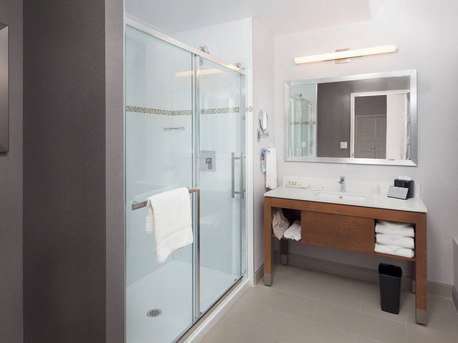 Un baño moderno con cabina de ducha de vidrio, un lavabo con espejo y una obra de arte enmarcada en la pared.