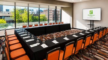 A conference room with a long table, orange chairs, and a city view through large windows.