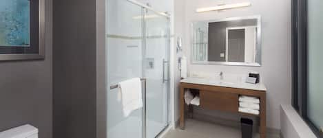 A modern bathroom with a glass shower enclosure, a wooden vanity, and a large mirror.