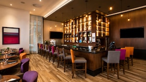 Zona de bar con mostrador de madera, distintas opciones de asientos y un televisor montado en la pared.