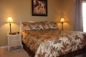 Une chambre à coucher avec une couvre-lit à motifs floraux, deux lampes de chevet, une table de chevet avec des tiroirs et un tableau encadré au mur.
