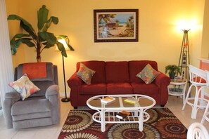 A living room with a red sofa, a grey armchair, a white coffee table, and a patterned rug.