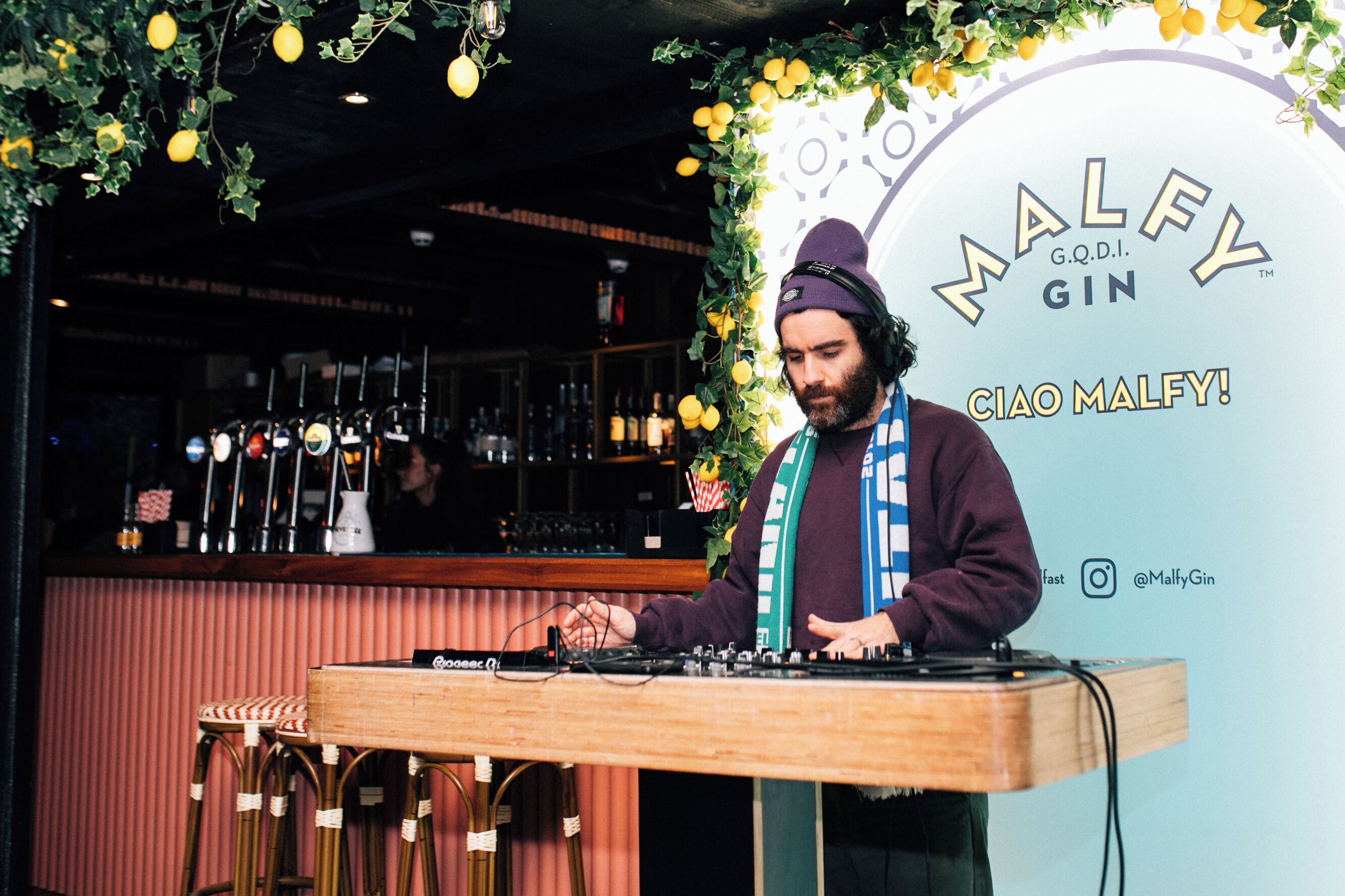 Un bar amb un espai per a DJ, tamborets i un cartell que diu 'Malley Gin'.