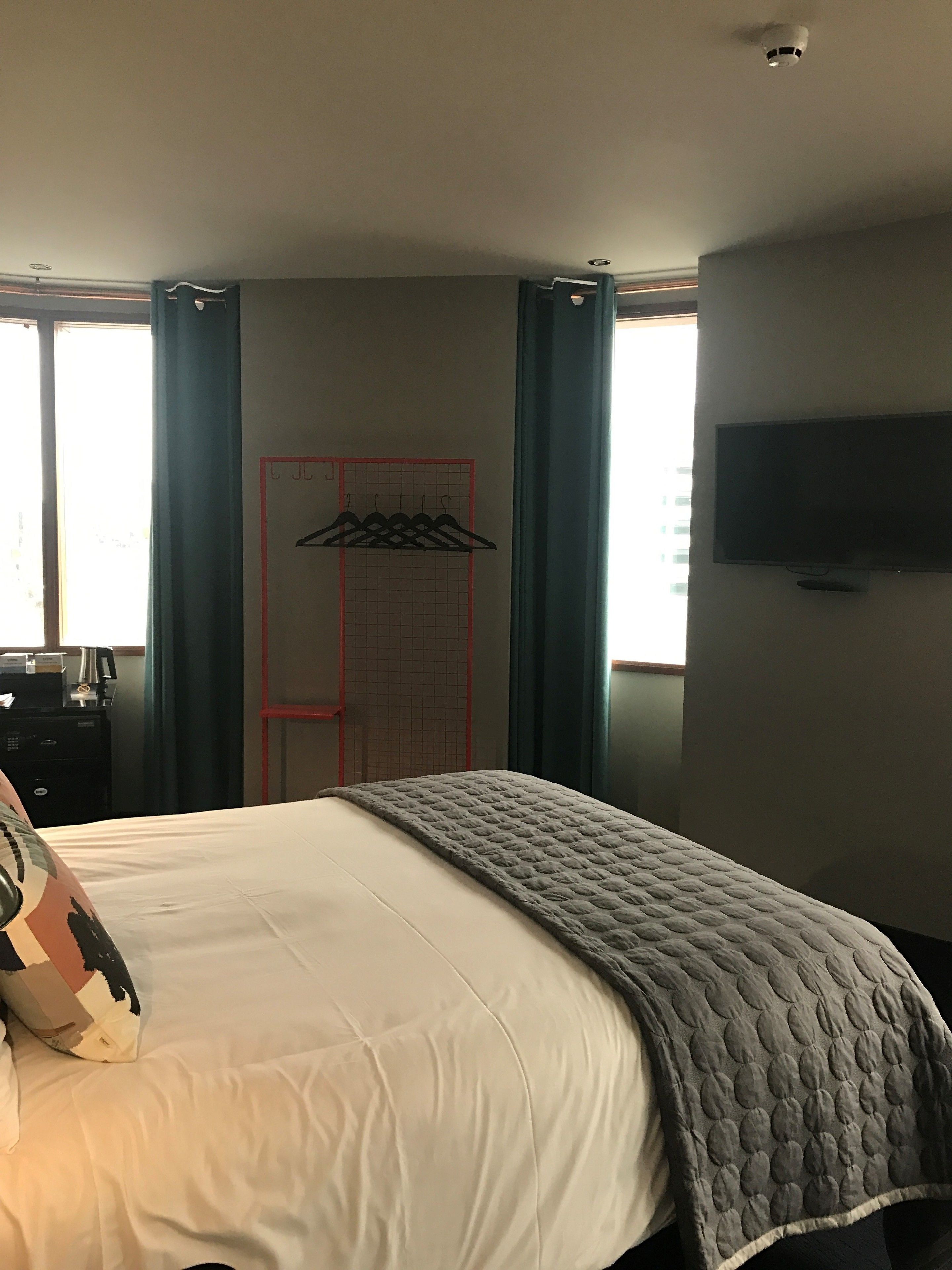 A hotel room with a bed, a TV mounted on the wall, and a window with curtains.
