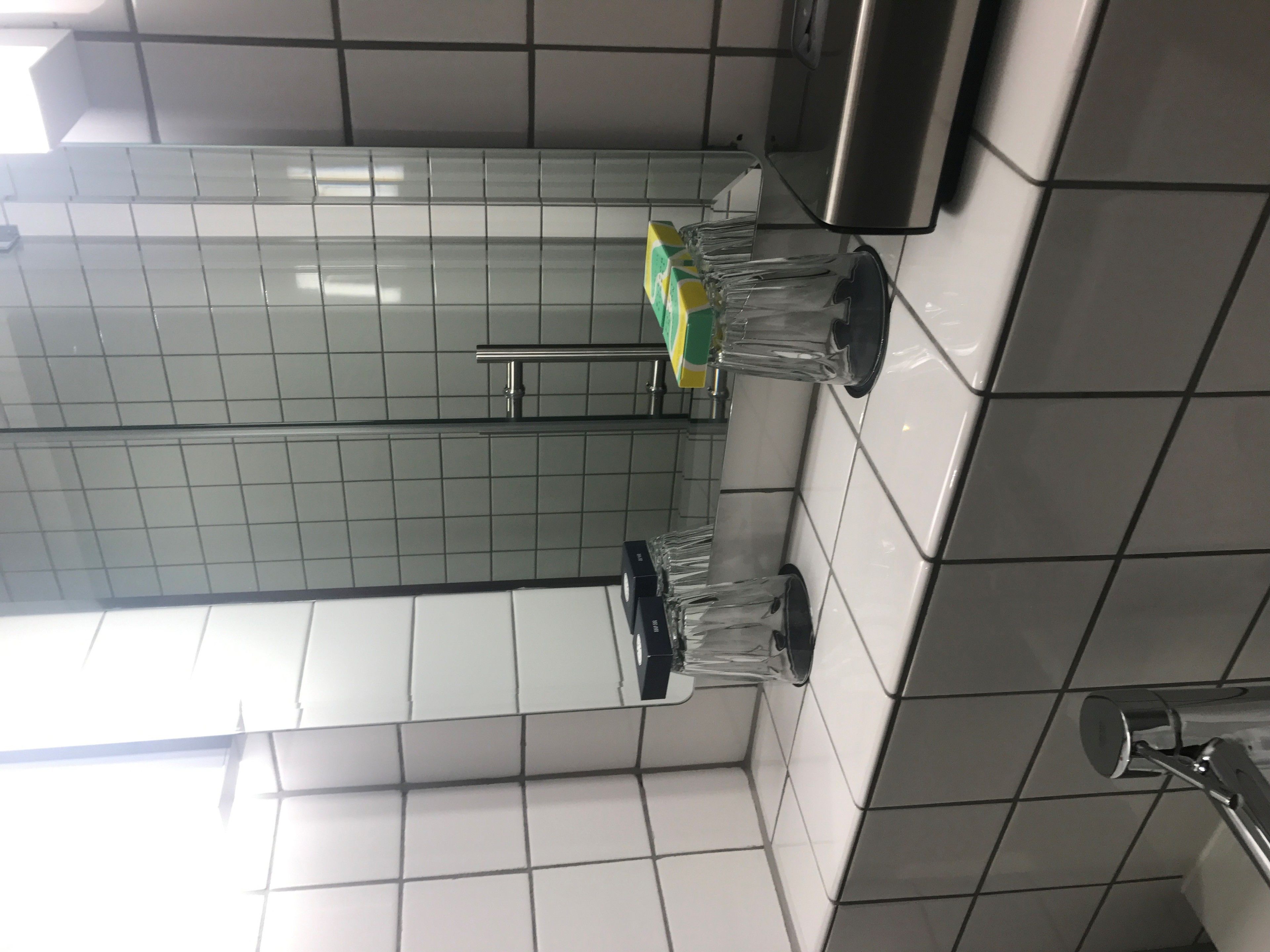A tiled bathroom with a hand dryer, a towel rack, and a mirror.