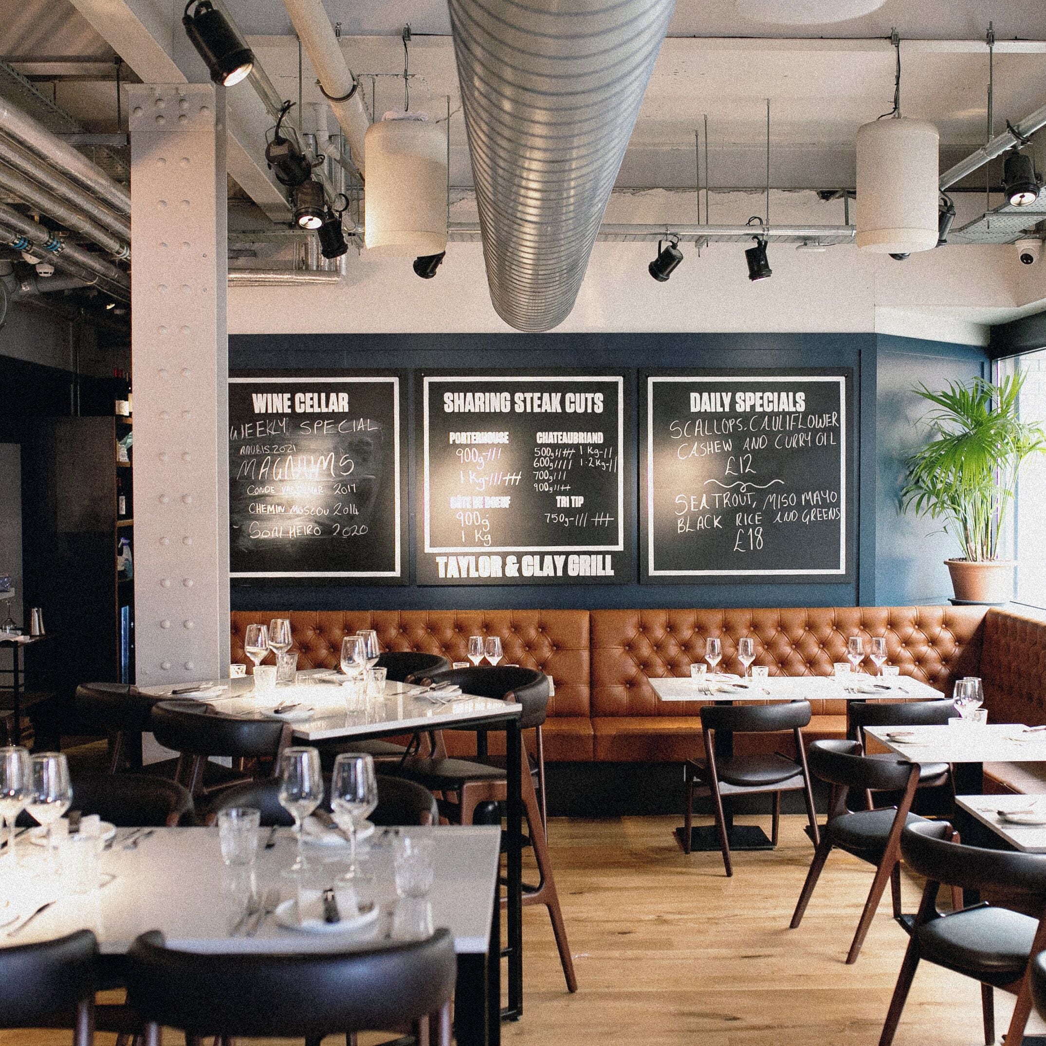 Un interior de restaurante con mesas dispuestas para comer, un menú en una pizarra y una planta en maceta.