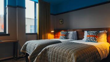 A hotel room with two beds, a window with curtains, a bedside table, and a wall-mounted picture.