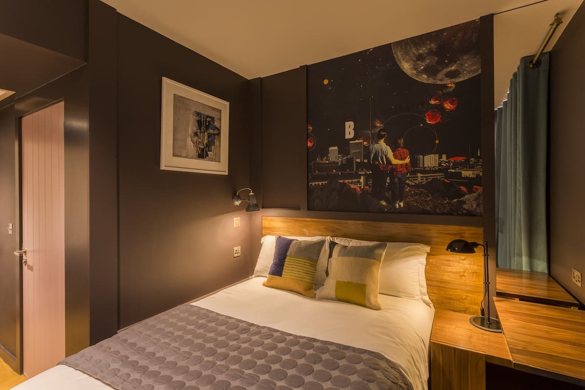 A modern hotel room with a large bed, a wooden headboard, a night sky mural, and a framed picture on the wall.