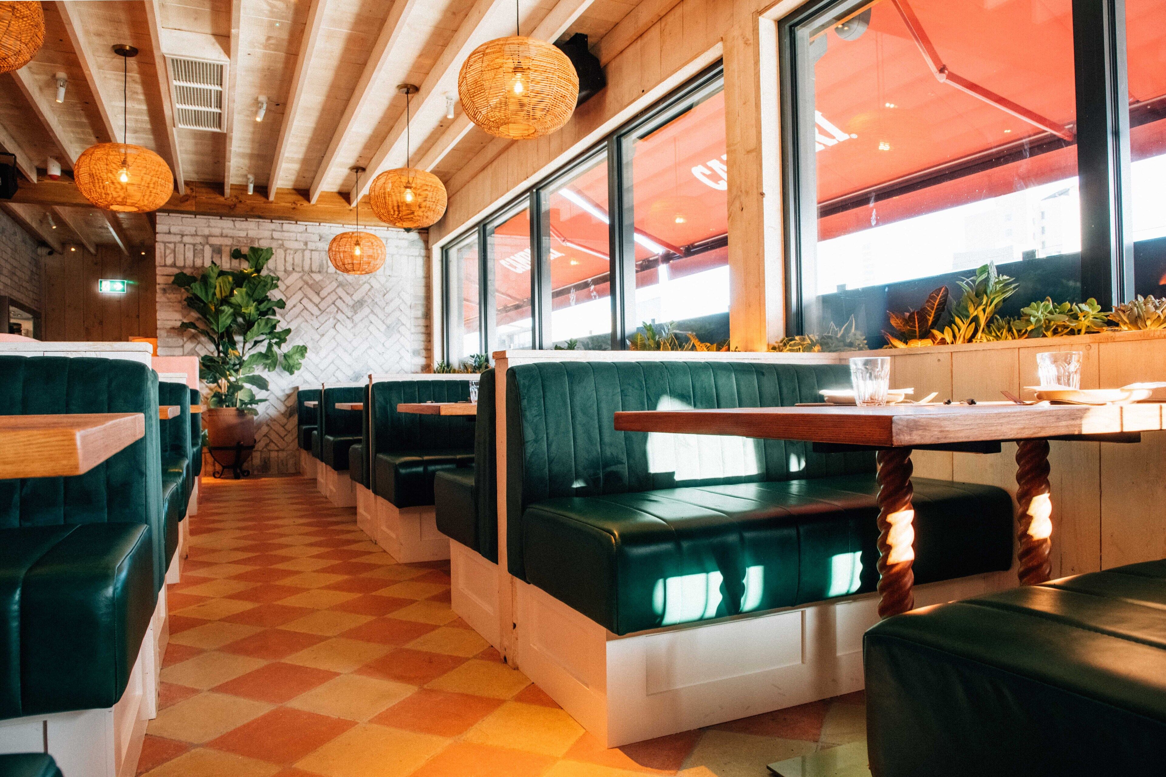 A restaurant with green booths, wooden tables, and hanging wicker lamps.