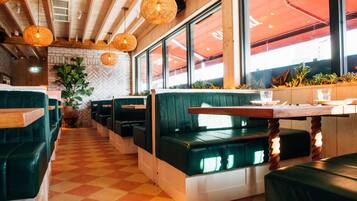 A restaurant with green booths, wooden tables, and hanging wicker lamps.