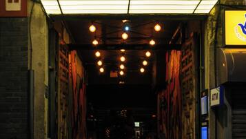 A narrow alleyway with a marquee sign reading "BULLITT" overhead, flanked by brick walls and potted plants.