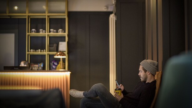 A person sitting on a chair in a room with a reception desk and shelves in the background.