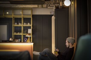 Una persona sentada en una silla en una habitación con una mesa de recepción y estanterías al fondo.