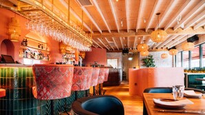 Een restaurant met houten balken in het plafond, tafellinnen met patroon en hangende lampen.