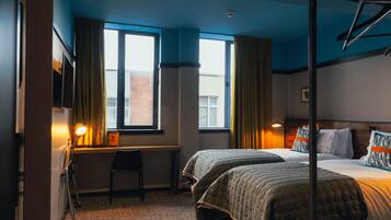 Quarto de hotel com duas camas, uma mesa, uma cadeira e uma janela com cortinas.