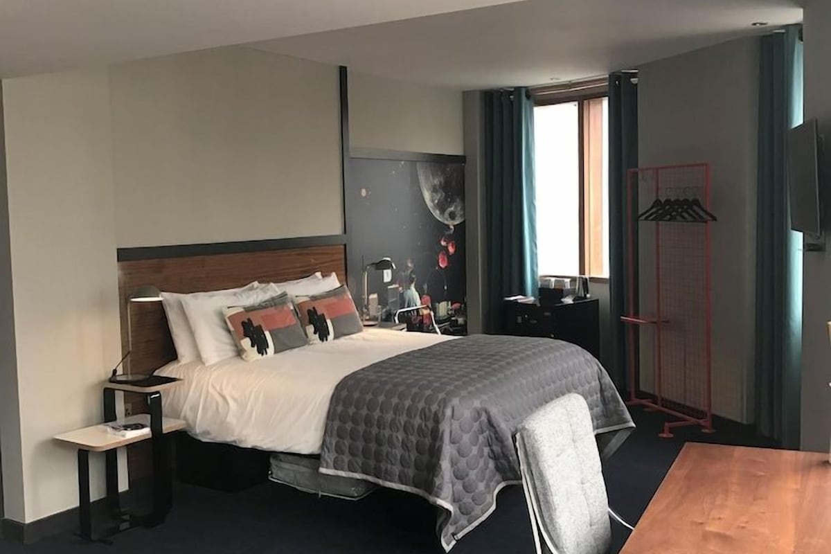 A modern hotel room with a bed, bedside table, and a small wooden table.