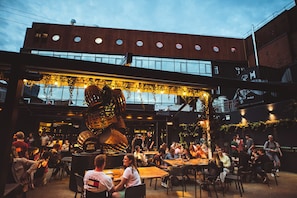 An outdoor dining area with tables and chairs, a large decorative structure, and a building with multiple windows in the background.