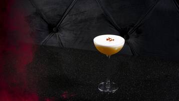A cocktail in a martini glass on a black table with a dark, textured background.