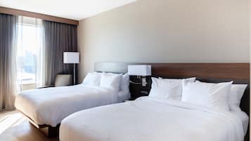 Een hotelkamer met twee bedden, een nachtkastje met een lamp, een stoel en een groot raam met gordijnen.