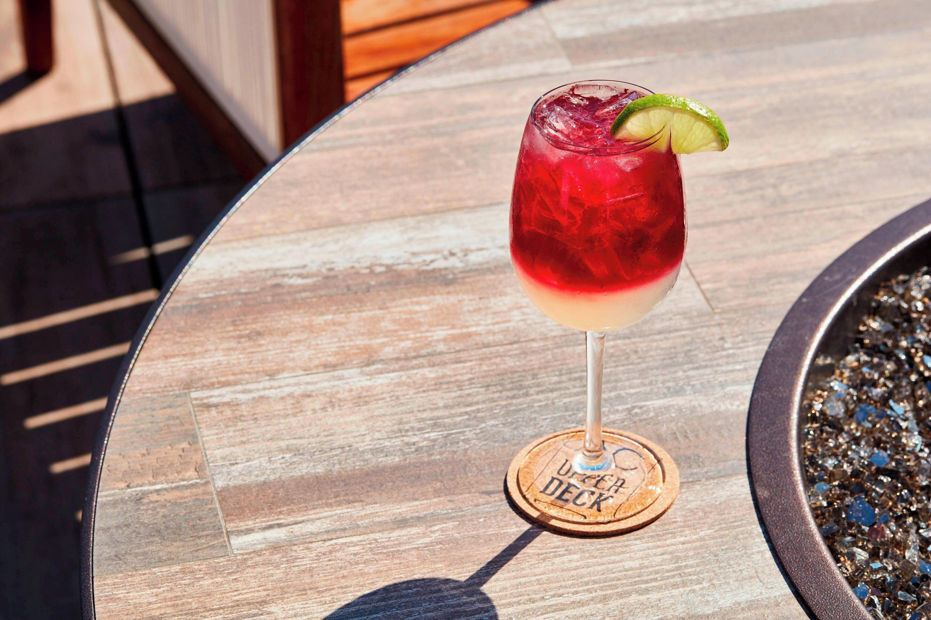 A cocktail glass with a lime garnish on a wooden coaster labeled "USER DECK" on a table.