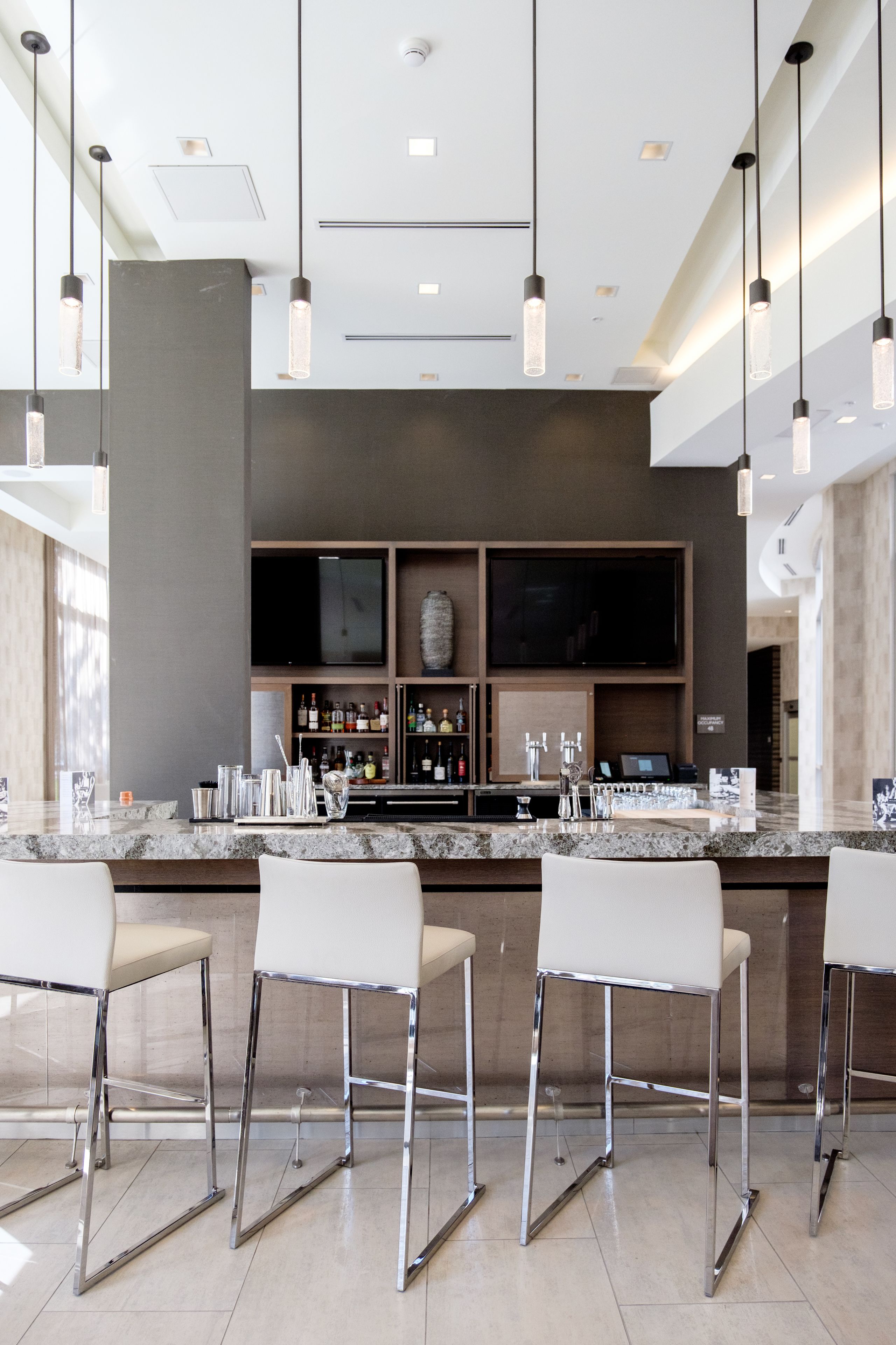 A modern bar area with a marble countertop, bar stools, and overhead lighting.