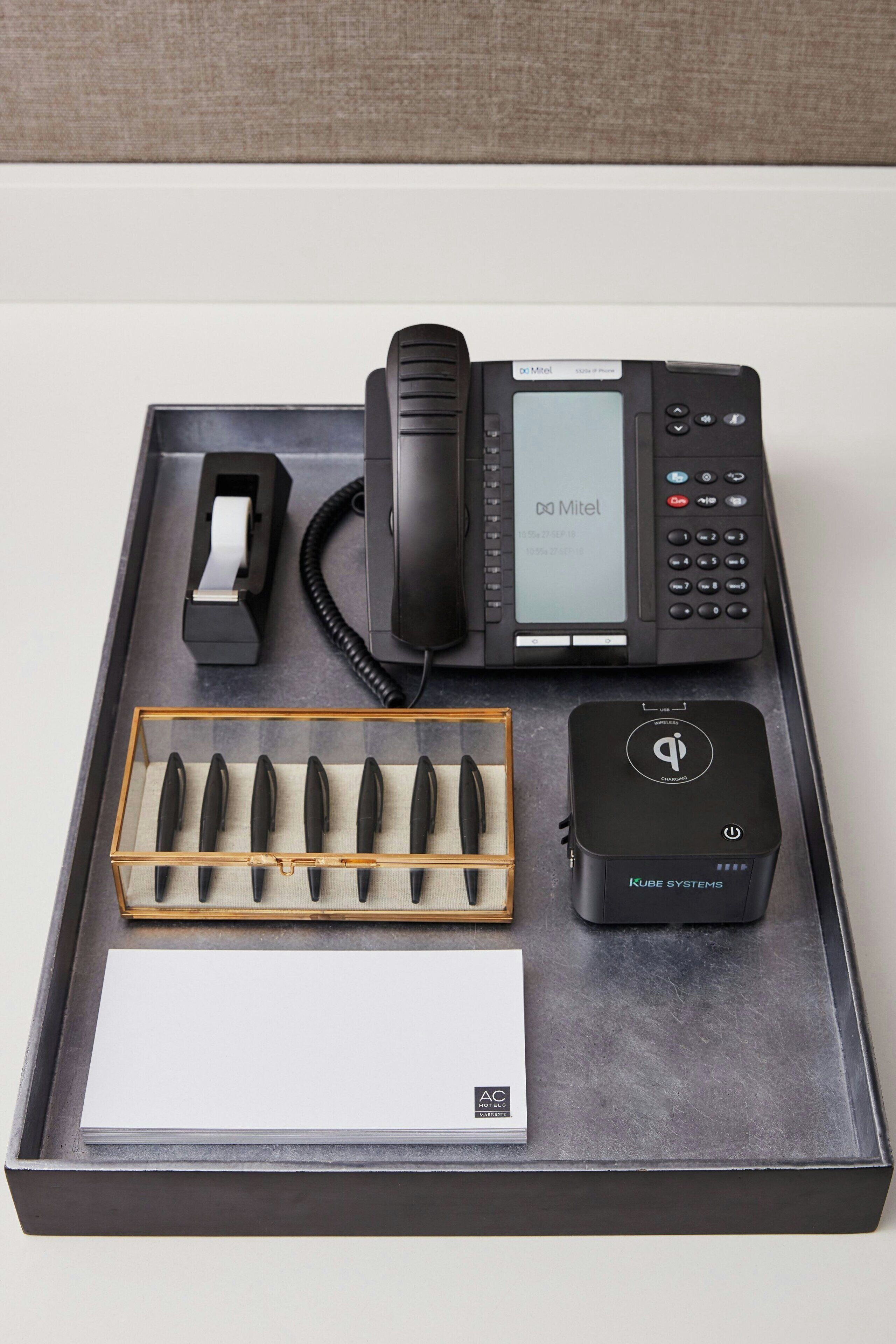 Et skrivebord med telefon, tape dispenser, penneholder, stikdåse og en hvid kasse.