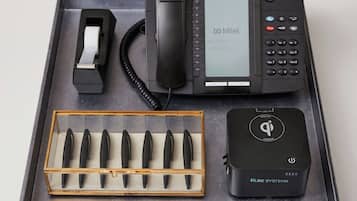Et skrivebord med telefon, tape dispenser, penneholder, stikdåse og en hvid kasse.