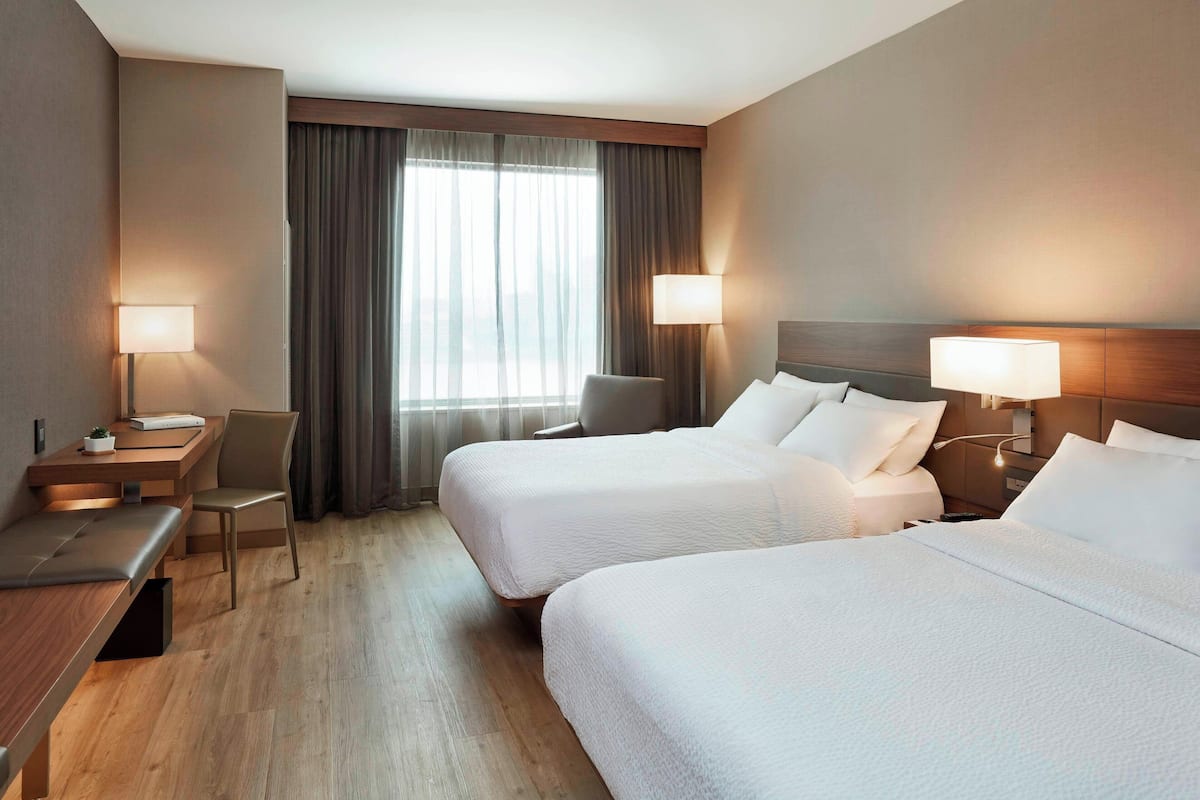 Ein Hotelzimmer mit zwei Betten, einem Schreibtisch, einem Stuhl und einem Fenster mit Vorhängen.