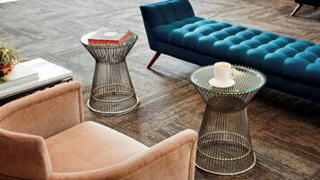 A modern living room with a blue sofa, a pink armchair, and two unique wire tables with books and a candle.