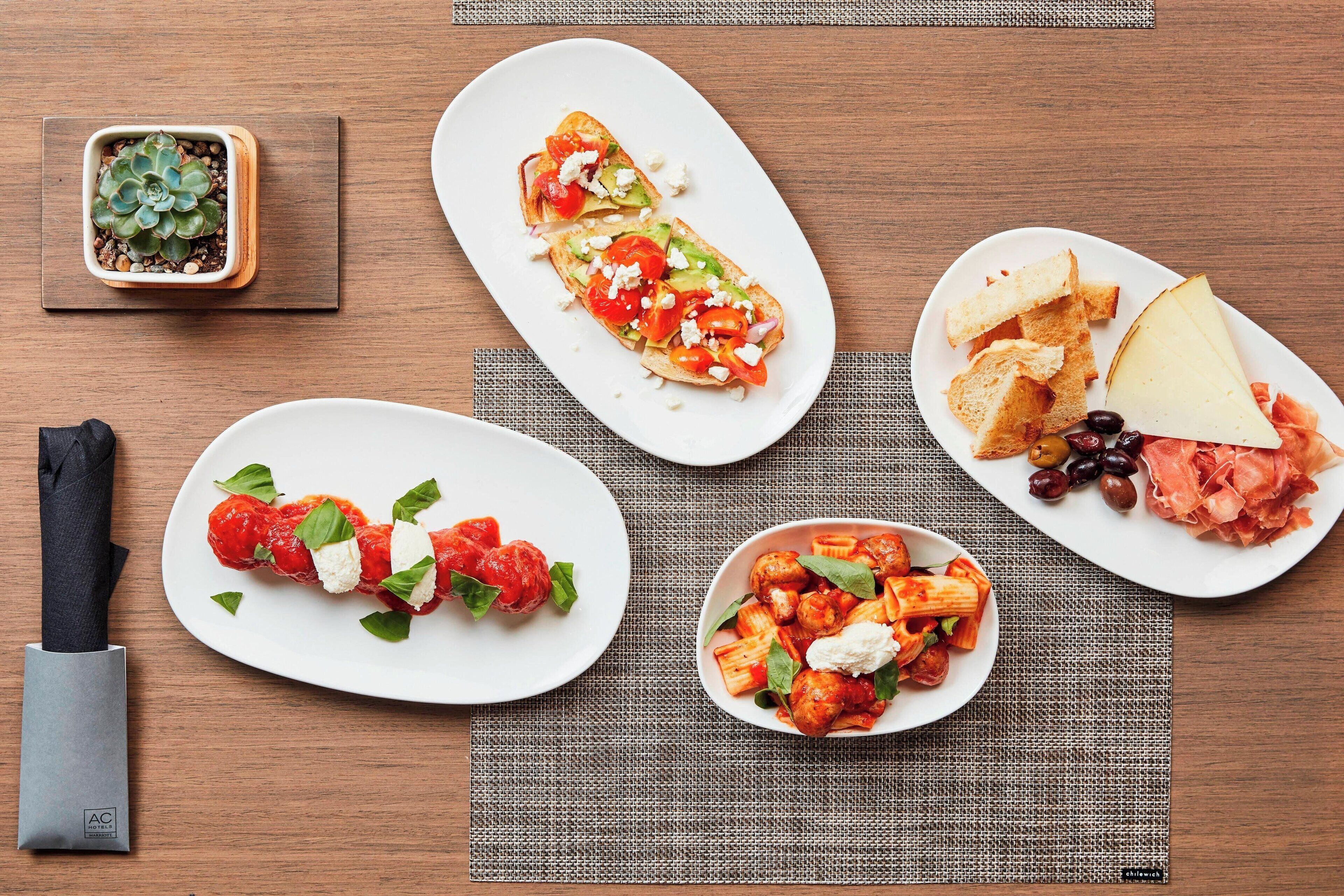 A wooden table with four plates of food, a small potted plant, and a knife.