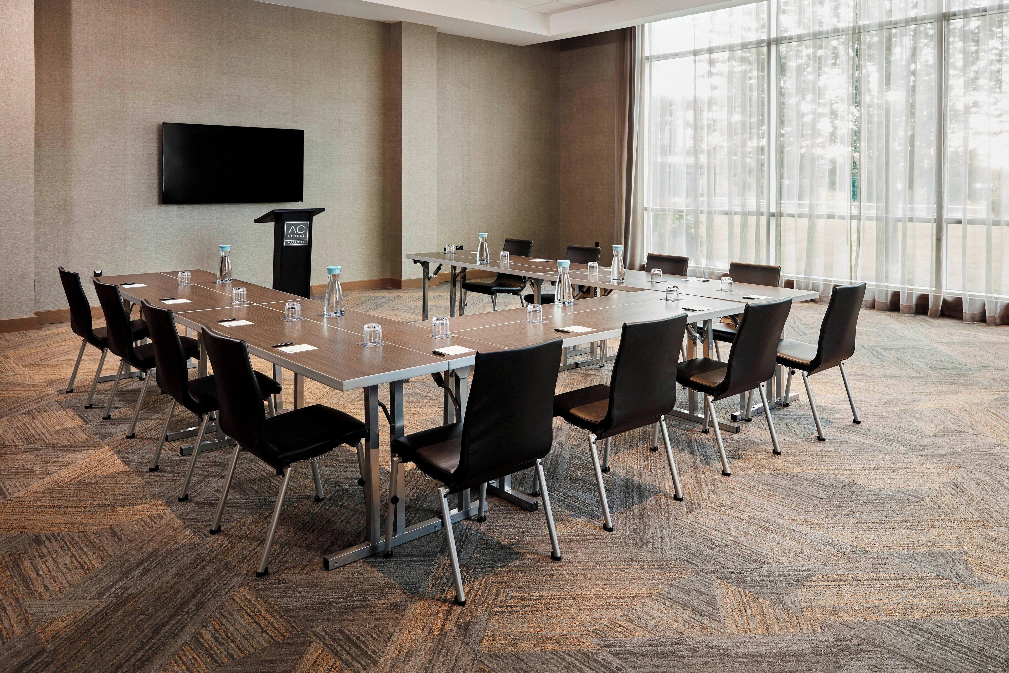 A conference room with a large table, chairs, a podium, and a TV screen.