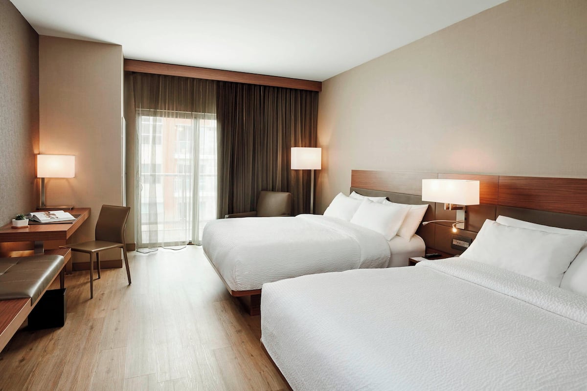 Ein Hotelzimmer mit zwei Betten, einem Schreibtisch, einem Stuhl und einem Fenster mit Vorhängen.