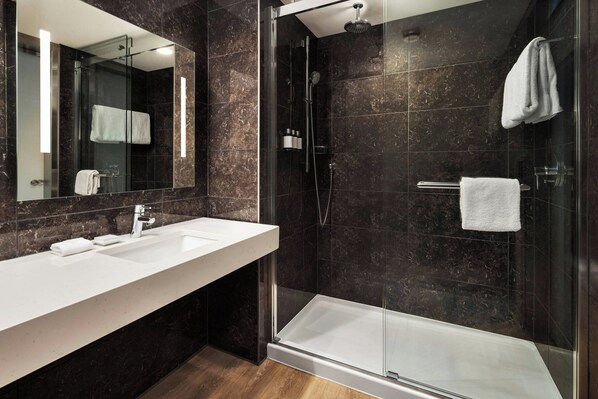 Un baño moderno con ducha envuelta en vidrio, un lavabo blanco y un espejo grande.