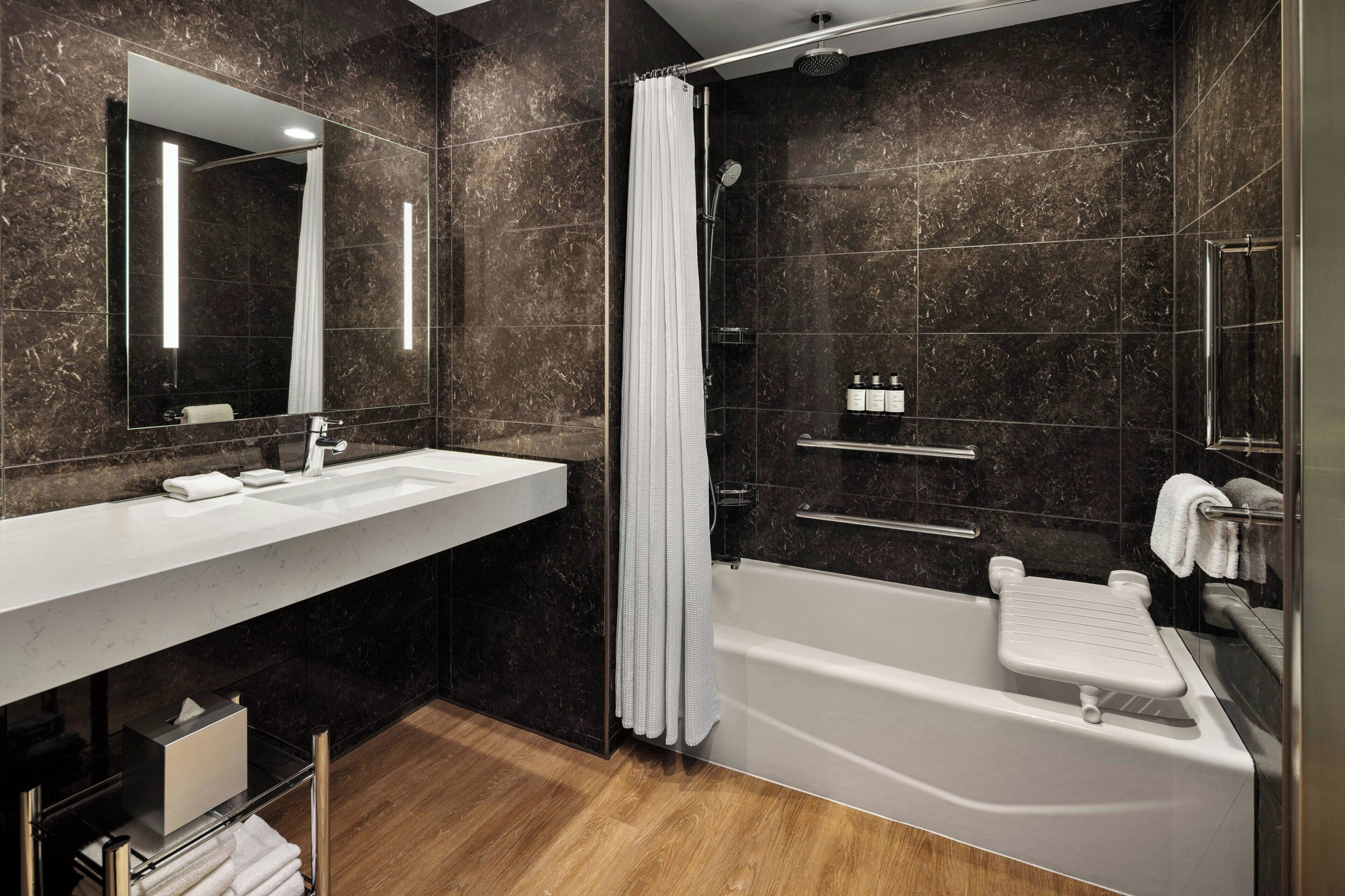A modern bathroom with a large mirror, a white bathtub, and a shower area.