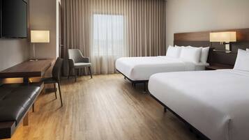 A hotel room with two beds, a desk, a chair, a TV, and a window with curtains.