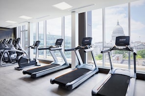 A gym with treadmills and elliptical machines, large windows with a cityscape view.